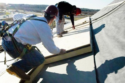 Two men with hard hats and safety harnesses install roof insulation
